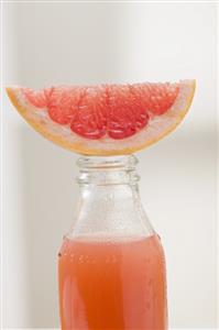 Pink grapefruit juice in bottle with fresh grapefruit wedge
