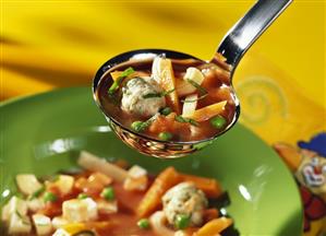 Noodle soup with dumplings on ladle over plate