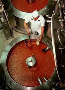 Worker taking sample from boiler in soup factory