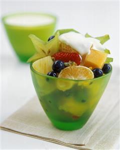 Fruit salad with a blob of cream in green glass bowl