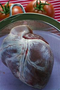 Raw beef heart in a sieve, tomatoes in the background