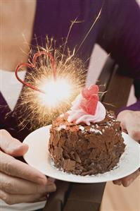 Woman holding small chocolate cake with sparkler