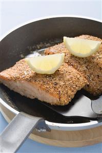 Fried salmon fillet with lemon wedges in frying pan