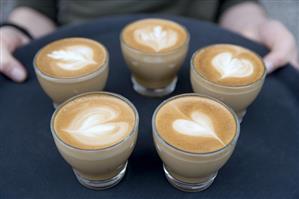 Woman carrying tray of cappuccino with heart-shaped milk froth