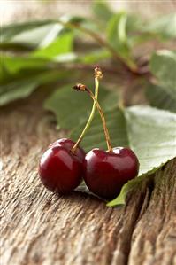 Two cherries with leaves on wooden background