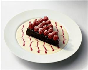 Slice of Chocolate Tart Topped with Fresh Raspberries in a Decorative Sauce on White Plate