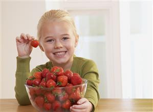 Young girl in kitchen with a bowl of strawberries smiling