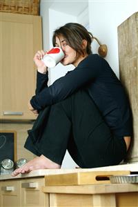 Mujer vestida de negro sentada en el mueble de la cocina, con una taza de corazones.